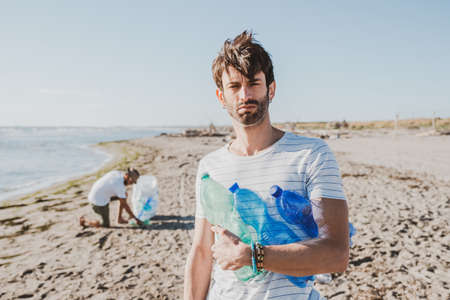 Group of activist friends collecting plastic waste on the beach. People cleaning the beach, with bags. Concept of environmental conservation and ocean pollution problemsの写真素材