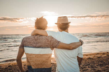 Two friends hug each other looking sunset on the beach. Friendship and love conceptの写真素材
