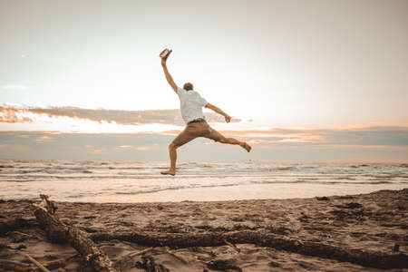 Happy boy enjoying summer holidays on beach at sunset - Young man jumping on the beach at the sunrise - Vacations conceptの写真素材