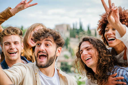 Friends students relaxing outside taking group selfies and smiling on smartphone, on the street