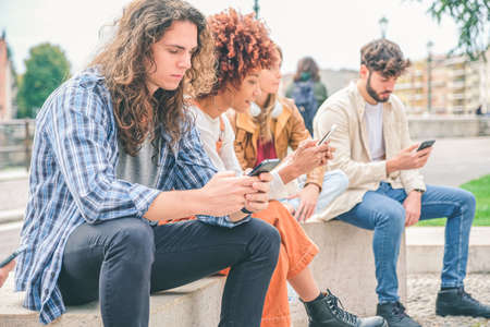 Multicultural group of friends using mobile phones - Students sitting in a row and typing on...