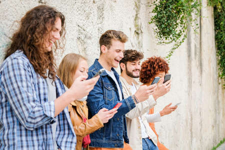 Multicultural group of friends using cellphones outdoors - Students browsing internet holding mobile...
