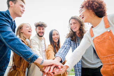 Portrait of happy university friends stacking hands together, showing unity and togetherness -...