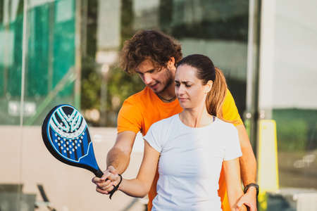 Young teacher is monitoring teaching padel lesson to his student - Coach teaches girl how to play padel on the outdoor tennis courtの写真素材