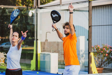 Young teacher is monitoring teaching padel lesson to his student - Coach teaches girl how to play padel on the outdoor tennis courtの写真素材