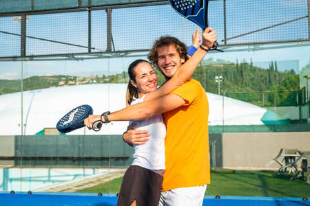 Portrait of two smiling sportsman's posing on padel court outdoor with rackets - Padel players looking at camera and embracing after win a padel matchの写真素材