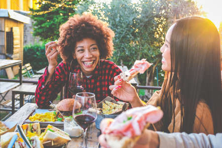 Group of multiethnic friends living healthy lifestyle and smiling and joking while drinking red wine at outdoor pub restaurant - Young people toasting with wine glass during happy hour at barの写真素材