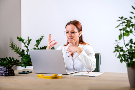 Portrait of female nutritionist in medical gown using laptop for online consultation via video chat...