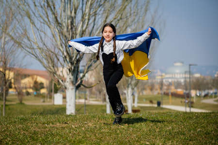 Happy Ukrainian girl running at the park waving the yellow and blue national flag. Concept of love for Ukraine. Independence, flag, Constitution Day of Ukraineの写真素材