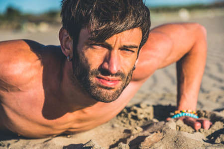 Close-up sexy portrait of handsome male model topless on the beach at sunrise - Fitness man doing...