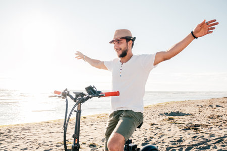 Young man on bicycle having fun with electric bike - carefree boy having fun and smiling on bicycle on the beach on a sunny day - freedom conceptの写真素材