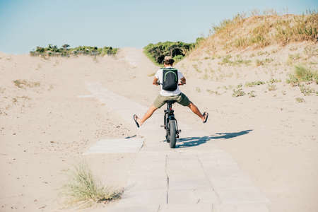 Young man on bicycle having fun with electric bike - carefree boy having fun and smiling on bicycle on the beach on a sunny day - freedom conceptの写真素材