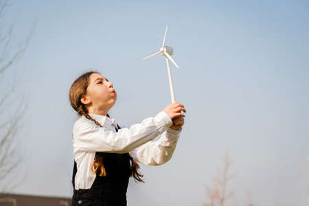 Closeup of little girl blowing a wind turbine toy and studying how green energy works from a young age - Concept of future generation and enewable Energyの写真素材
