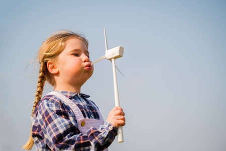 Closeup of little girl blowing a wind turbine toy and studying how green energy works from a young age - Concept of future generation and enewable Energyの写真素材