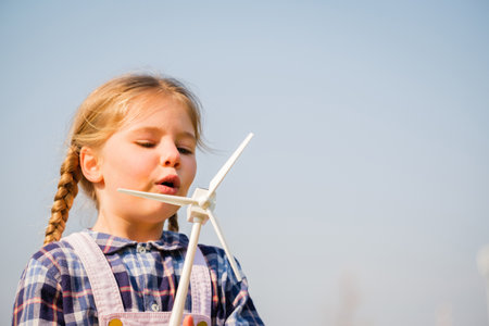 Closeup of little girl blowing a wind turbine toy and studying how green energy works from a young age - Concept of future generation and enewable Energyの写真素材