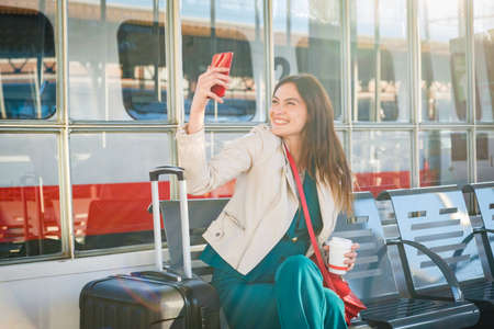 Young business woman waiting for the train sitting at the waiting room of train station - Cheerful and happy traveler talking on the smartphone while waiting for the trainの写真素材
