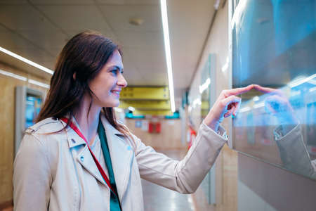 Young girl pointing with his hand and looking for the train on the departures and arrivals board -...