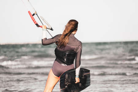 Young beautiful sporty woman ready for kite surfing in wetsuit kiting on beach coast - A young girl kitesurfer prepares to enter the sea with her boardの写真素材