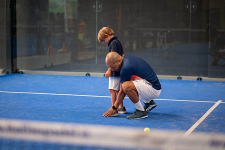 Monitor teaching padel class to child, his student - Trainer teaches little boy how to play padel on indoor tennis courtの写真素材