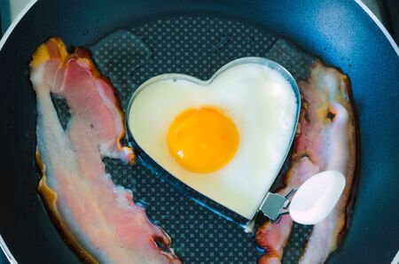 Frying an egg in the shape of a heart and bacon.の写真素材