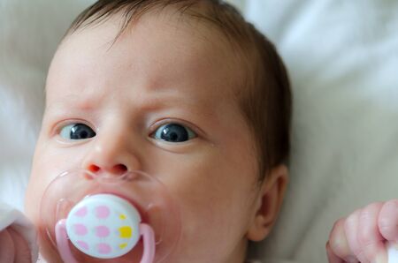 A newborn baby with a dummy lying down on white sheetsの写真素材