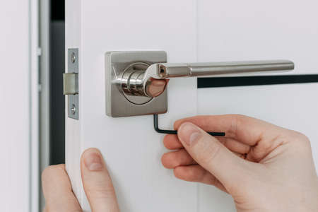 A locksmith is repairing an interior door lock. Close-up of male hands repairing or replacing an entrance door lock with a hex screwdriver. Selective focusの写真素材