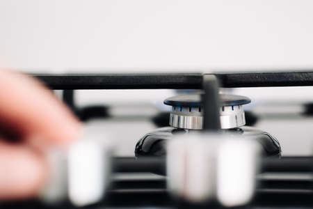 A gas cooker with regulators of level of a flame. A mans hand controls the power of the burner. Selective focusの写真素材