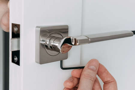 A locksmith install the door lock in the room. A locksmith adjust lock with hex key. Selective focusの写真素材
