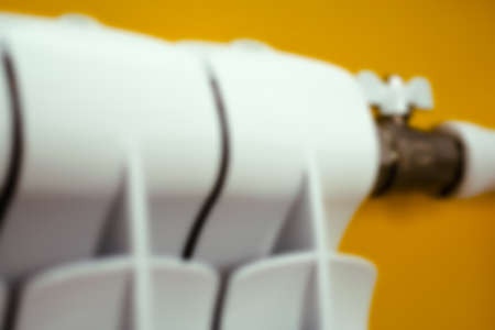 A heating radiator is out of focus. Blured. A heating radiator and a shut-off valve close-up on a yellow background. The concept of warm preservation. Selective focusの写真素材