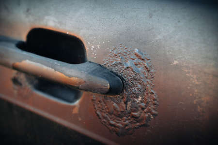 A fragment of the body of a rusty car door with a handle. Aggressive corrosion. Selective focus
