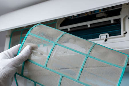A worker holds a dirty filter in his hand against the background of the internal unit of the split system. The concept of climate system maintenanceの写真素材
