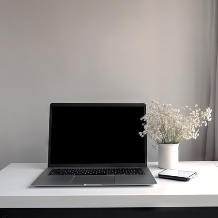 Workplace with blank screen laptop, smartphone and vase of flowersの素材