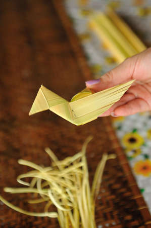 Unidentified person holding weave decoration resembling bird. It is made from young yellowing nipah leaves.の写真素材