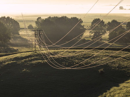 Power Lines held up by Pylons stretch across Farmland into the Foggy Field beyondの写真素材