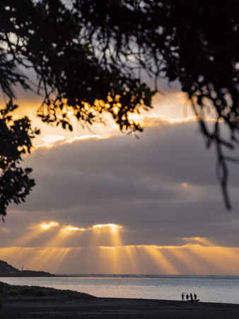 People Preparing for a Kayak or Canoe Adventure at Sunset on the Beach at Raglan Harbour New Zealand with Sun Rays in the Backgroundの写真素材
