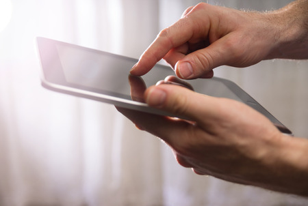 man holding tablet in the air while touching the screen with fingertip with a strong sun with a drama filter shallow depth of fieldの写真素材