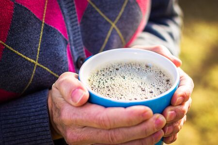 woman holding cup of coffee in the morning sun with a close-up of the cup shallow depth of fieldの写真素材
