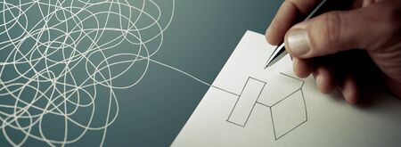 Expert business hand solving tangled line, outside the paper sheet on a blue deskの写真素材