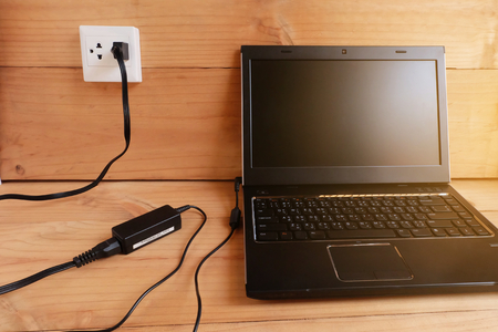 Plug in Adapter power cord charger of laptop computer On wooden floor With sun Warm lightの写真素材