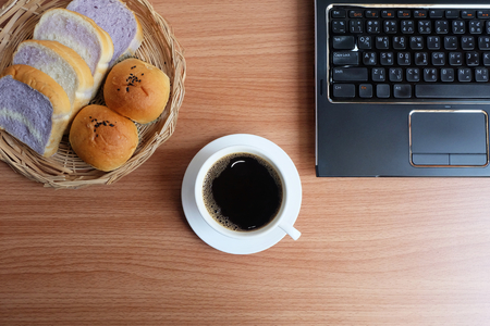 Black coffee in a white cup, bread, and laptop computer on wooden floor, Top viewの写真素材