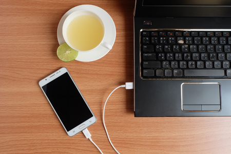 Plug in USB cord charger of the mobile phone with a laptop and freshly Lime juice in a white cup, on wooden floor, Top viewの写真素材
