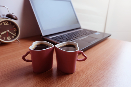 Black coffee in  two cups heart shape, and laptop computer on wooden floorの写真素材