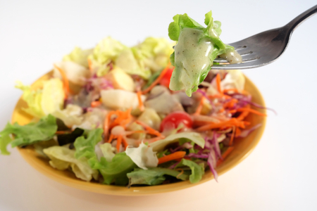 Close up salad and Caesar dressing with Black sesame on fork and blur focus salad on plate and white backgroundの写真素材