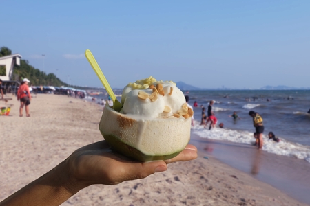 Woman hand holding Ice Cream in a fresh coconut cup Sprinkle with peanuts at the beach In summer Bang Saen.Chonburi, Thailandの写真素材