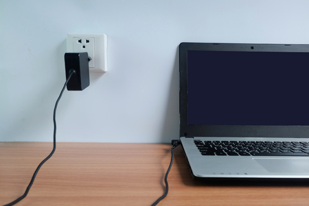 Plug in power outlet adapter cord charger on a white wall of the laptop computer on Wooden floor