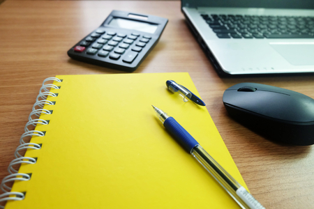 Yellow notebook with empty space and a pen,with laptop computer and wireless mouse on the desk...