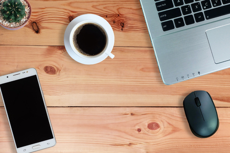 Black coffee in white cup and laptop computer and cactus and Mobile Phone or Smartphone with blank screen on wooden floor, Top view, copy spaceの写真素材