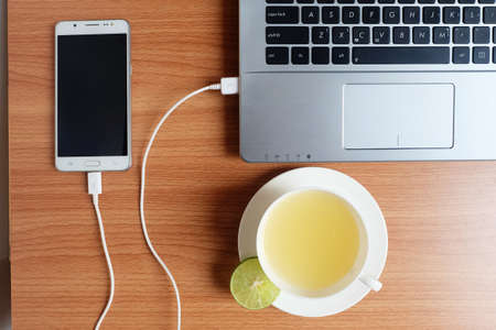 Plug in USB cord charger of the mobile phone with a laptop computer and freshly Lime juice in a...