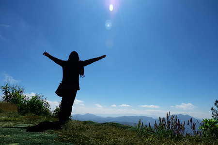Tourists Woman in a sweater standing on the cliff, with raised hands and looking to sky and mountain, Freedom and Tourism conceptの写真素材