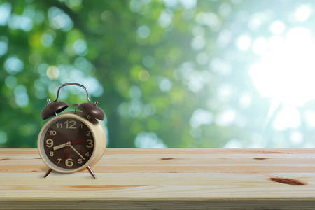 Alarm clock on wooden floor and green bokeh background with copy space, Morning wake up is bright air of nature for the new day concept.の写真素材